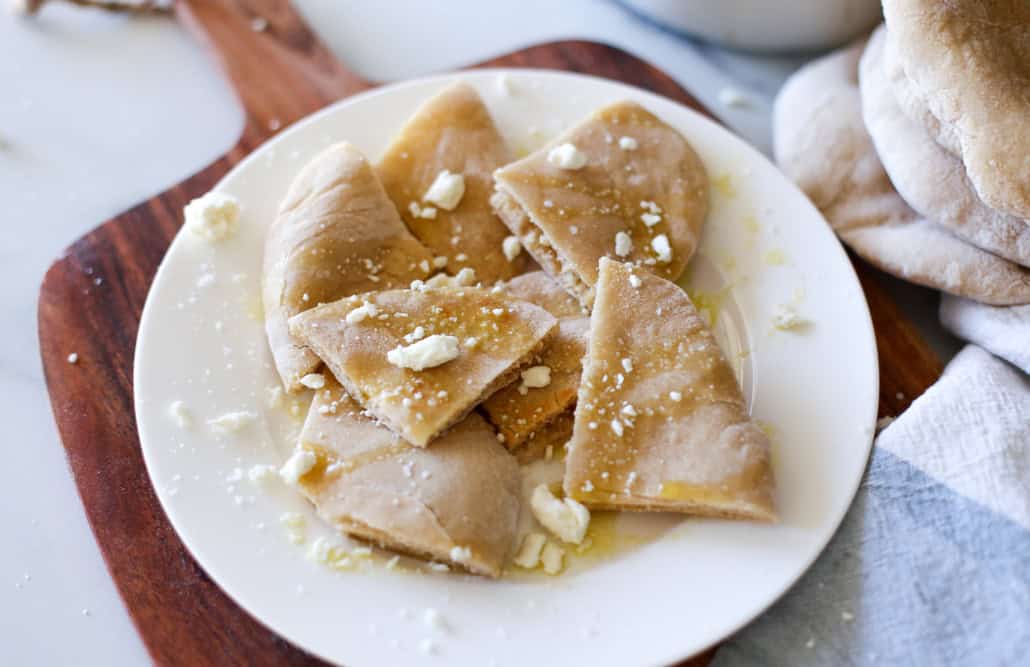 Whole wheat pita bread on a white plate with olive oil and feta cheese 