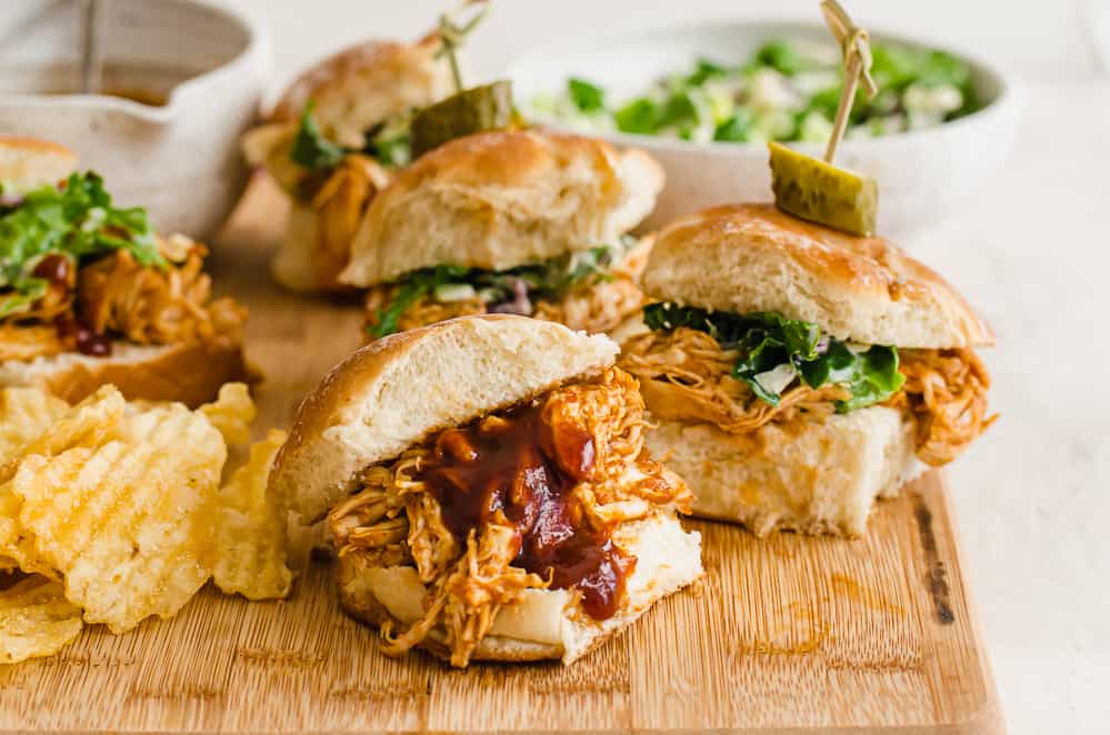 BBQ chicken sliders lined up on a wooden cutting board.