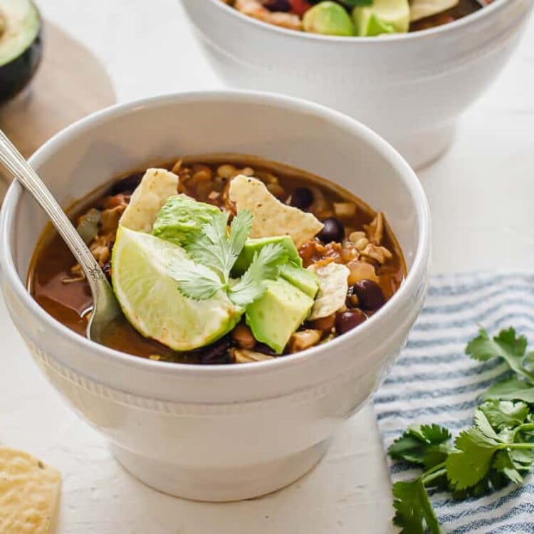 Chicken taco soup in a white bowl with toppings.