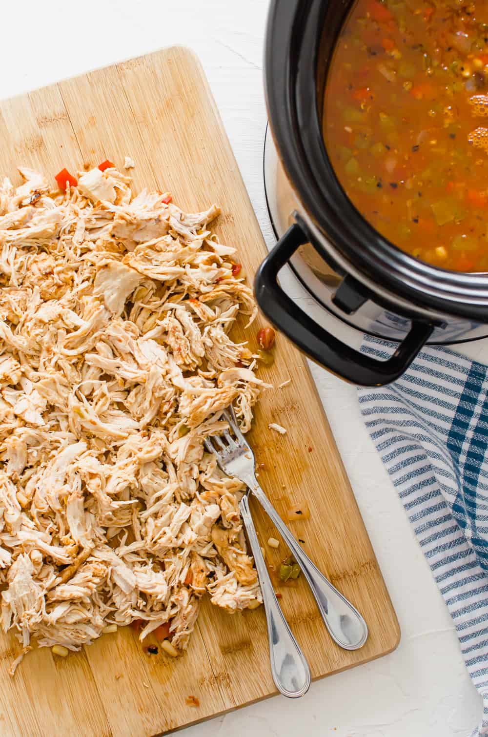 Shredded chicken on a wooden cutting board next to an Instant Pot with the rest of the chicken taco soup ingredients.