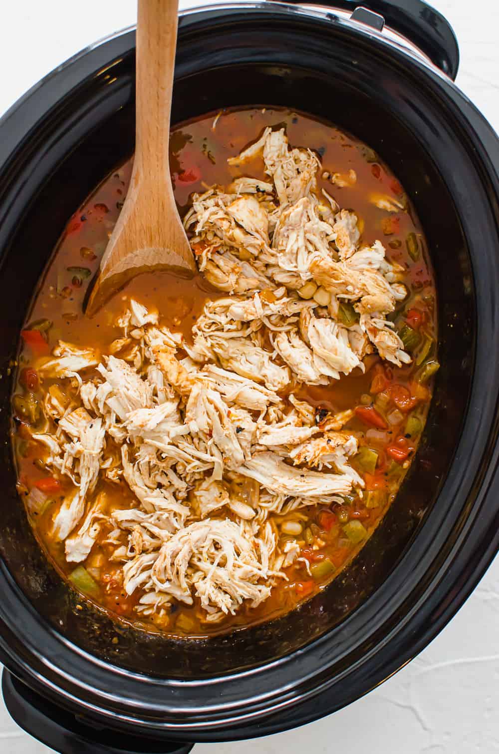 Shredded chicken placed on top of ingredients in a crock pot to make chicken taco soup.