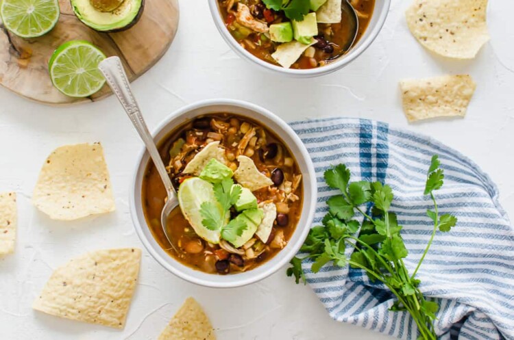 Chicken taco soup in a white bowl with toppings and tortilla chips around it.