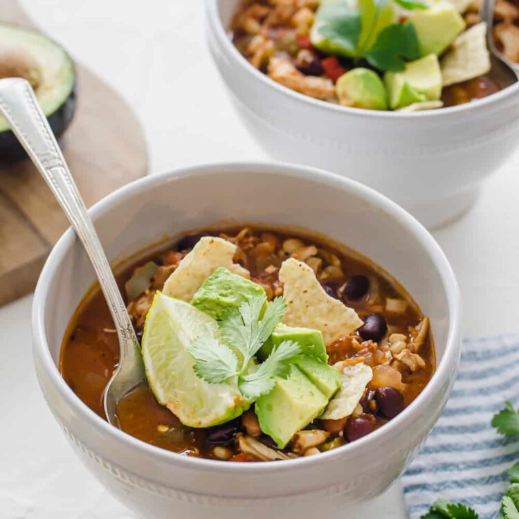Two white bowls of chicken taco soup with toppings on a table.
