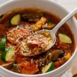 A bowl of pizza soup with a spoon lifting out a bite.