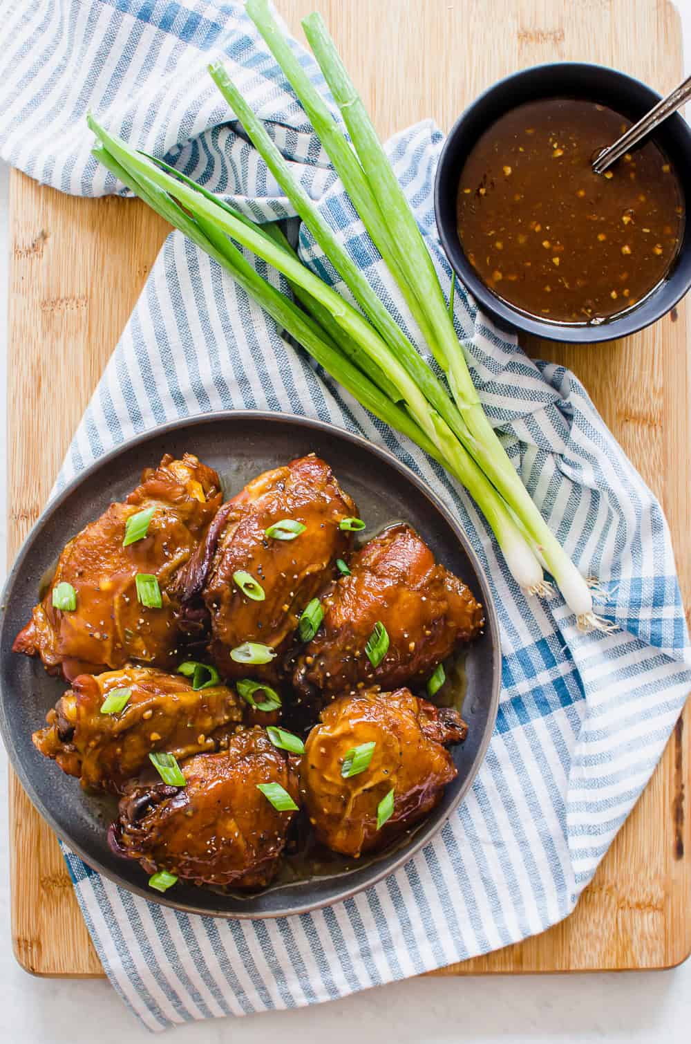 Teriyaki chicken thighs on a plate topped with green onion.
