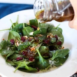 Parmesan balsamic vinaigrette being poured on a spinach salad.