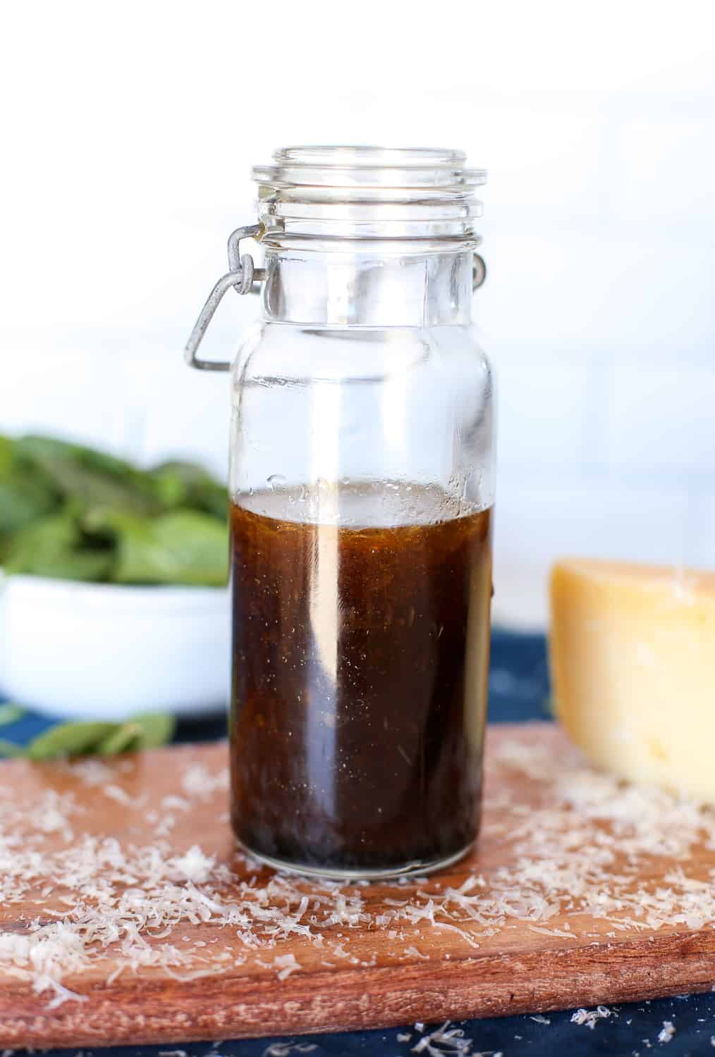 Parmesan balsamic vinaigrette in a glass bottle with a block of Parmesan and a spinach salad in the background.