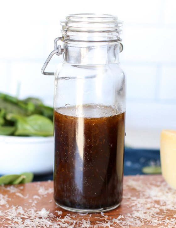 Balsamic Parmesan dressing in a jar with a bowl of baby spinach in the background.