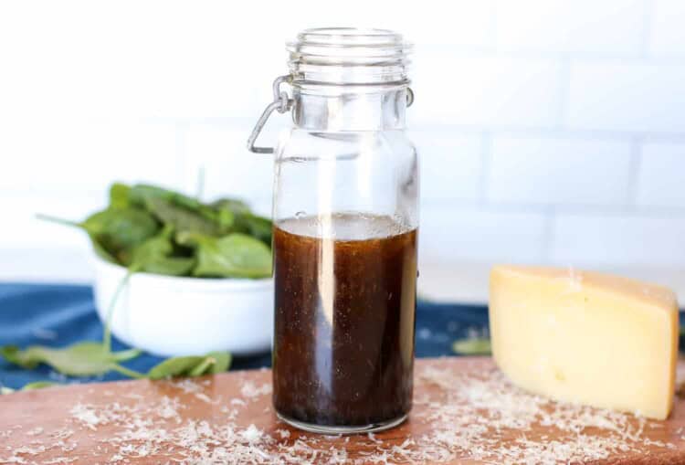 Balsamic Parmesan dressing in a jar with a bowl of baby spinach in the background.