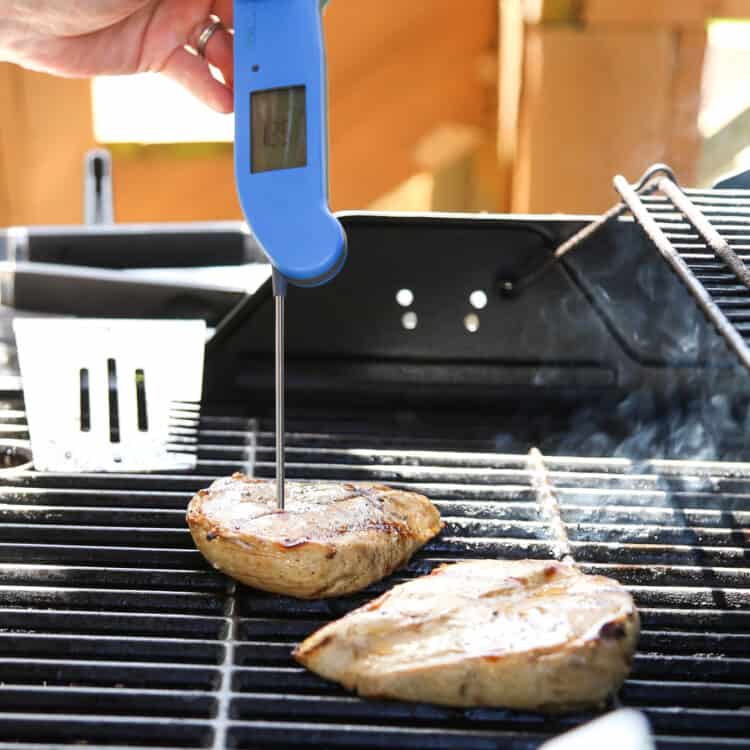 Meat thermometer being held inside a chicken breast on a grill.