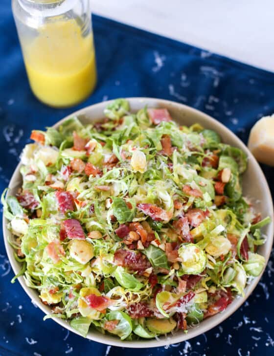 Shaved Brussels Sprouts salad with bacon on top and a jar of dressing next to it.
