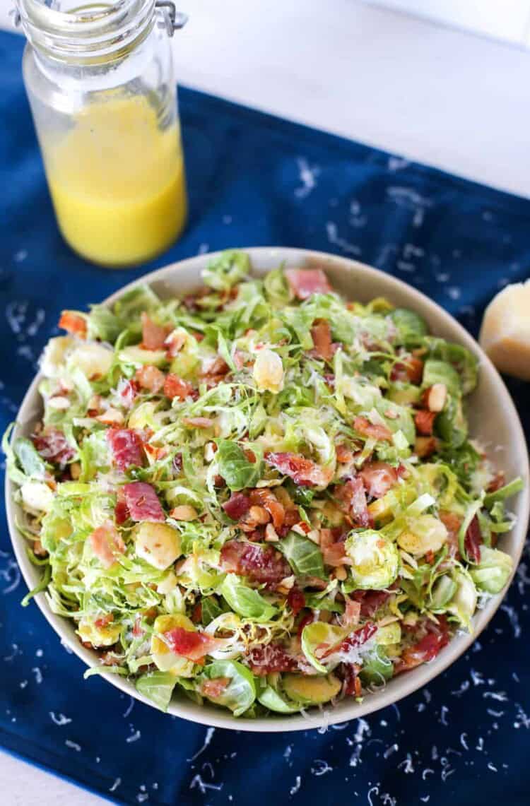 Shaved Brussels Sprouts salad with bacon on top and a jar of dressing next to it.