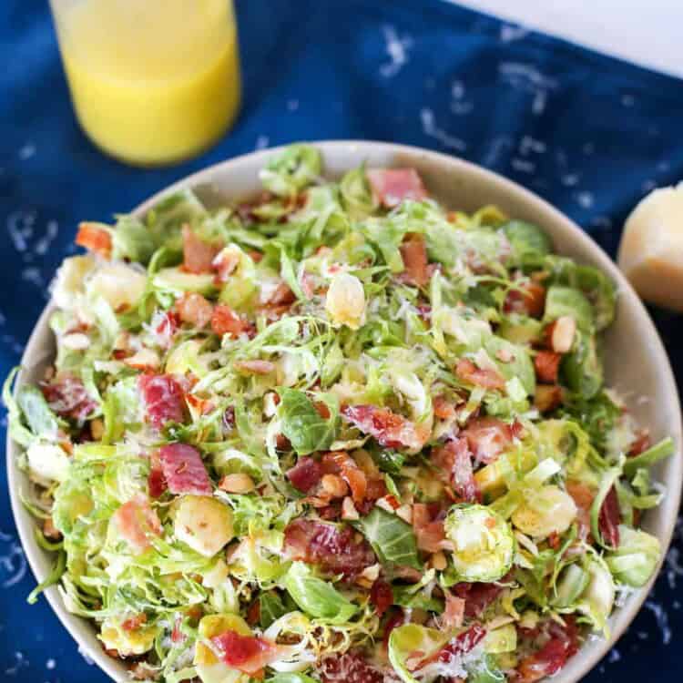 Shaved Brussels Sprouts salad with bacon on top and a jar of dressing next to it.