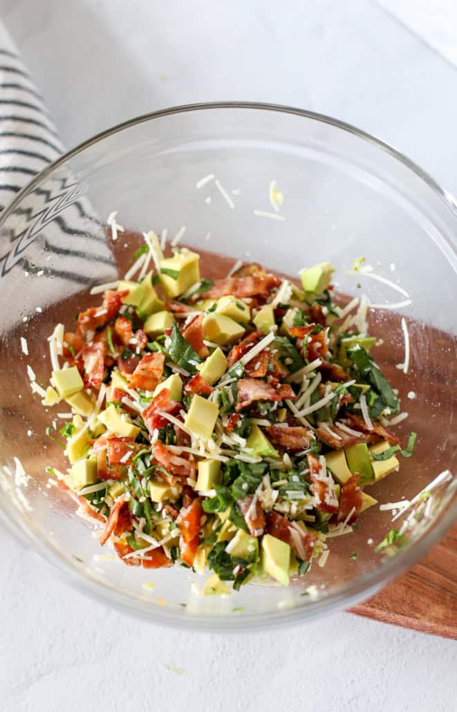 Ingredients for avocado pasta all stirred together in a glass bowl