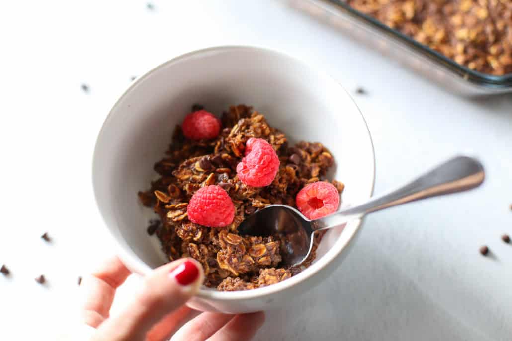 a hand holding a bowl of chocolate oatmeal with a spoon