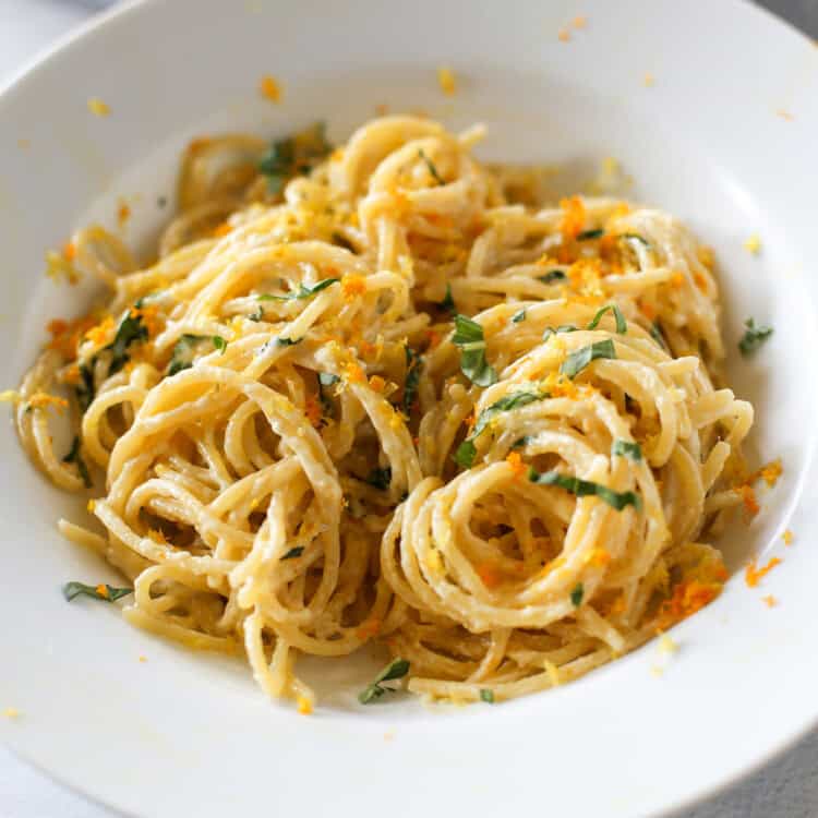 Creamy lemon pasta in a white bowl with fresh basil on top.