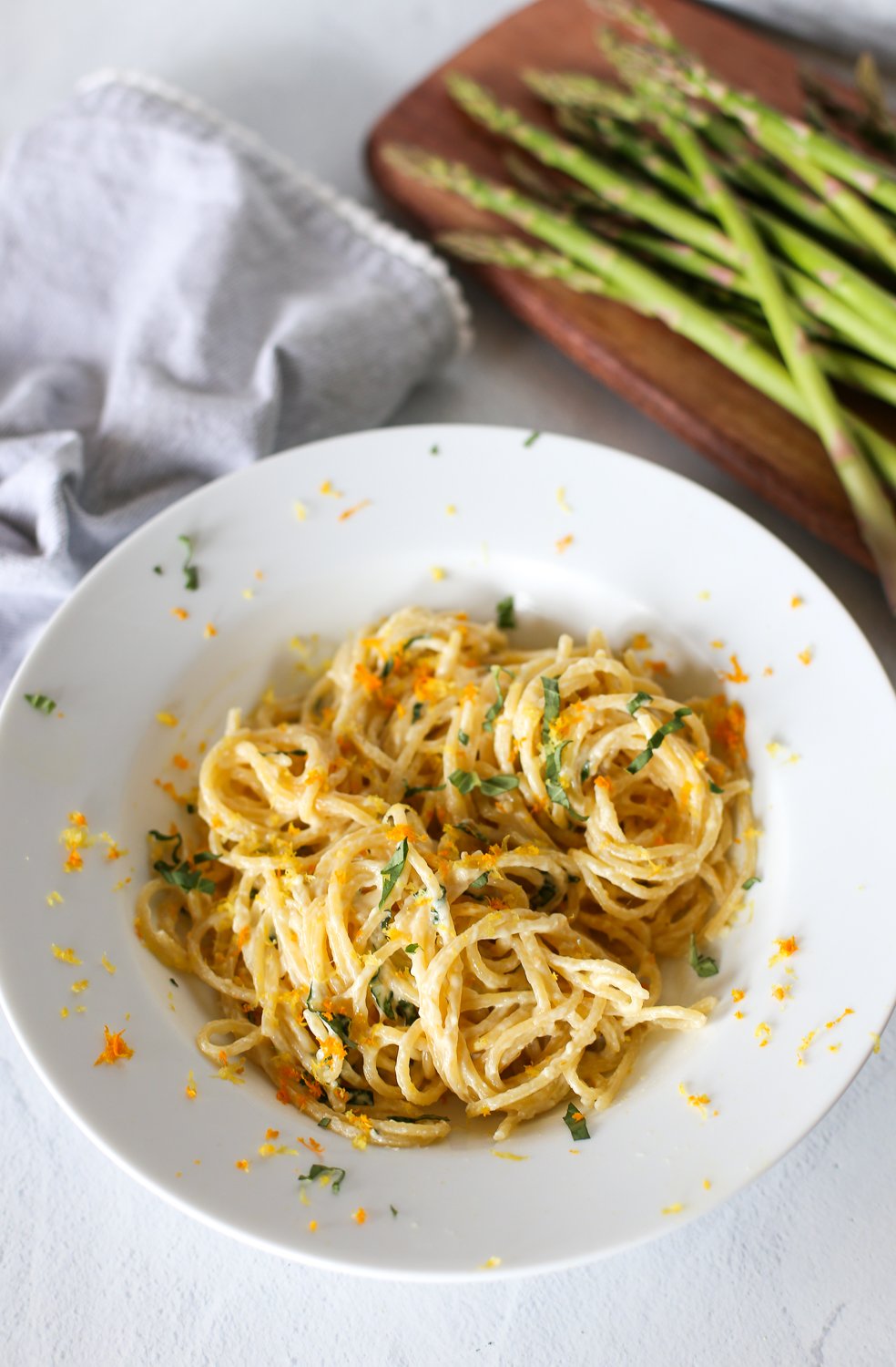 Creamy lemon pasta sauce in a white bowl with asparagus in the background.