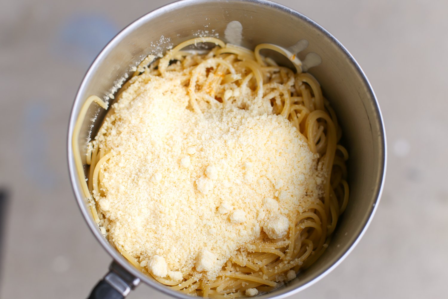 Parmesan cheese over the top of cooked pasta in a saucepan.