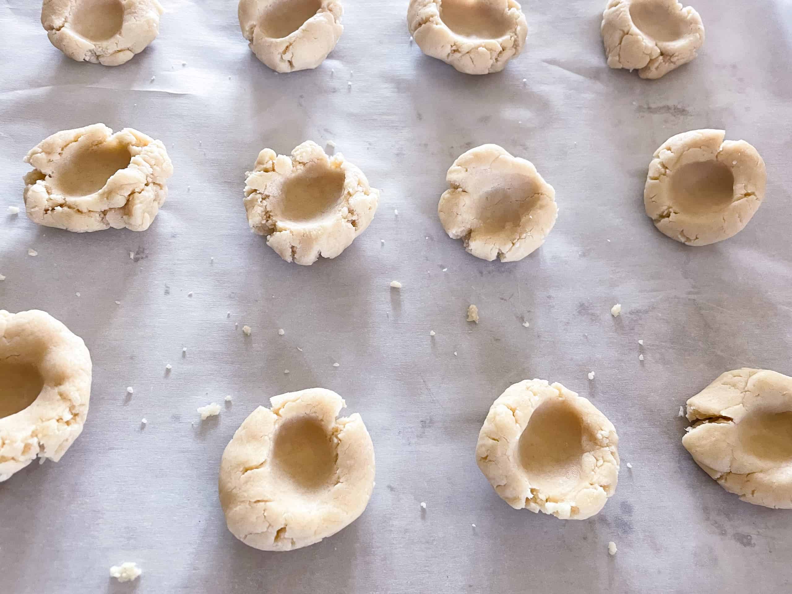 Shortbread cookie dough balls on parchment paper with thumb imprints in the middle of each.