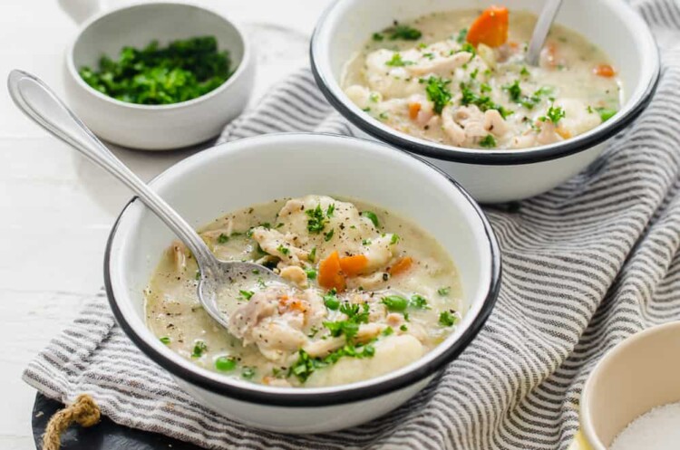 Two bowls of chicken and dumplings with spoons on a table.