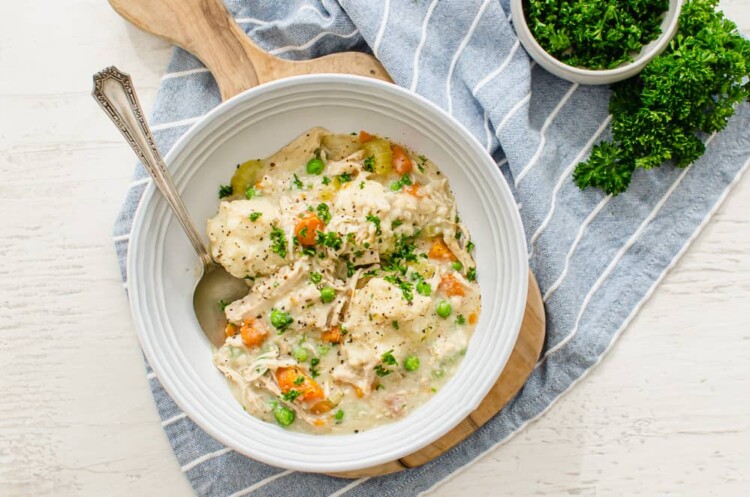 Chicken and dumplings served in a bowl with chopped parsley on top.