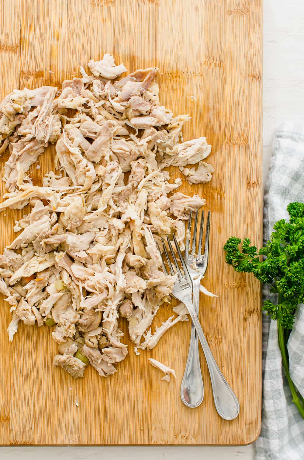 Shredded chicken on a cutting board with two forks sitting on it.