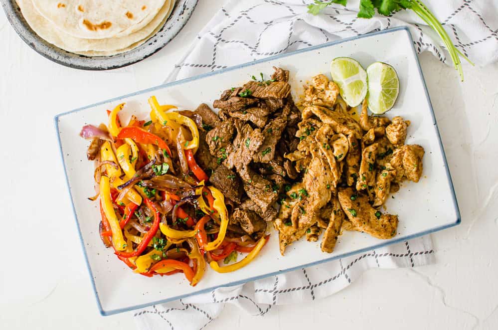 overhead shot of a serving platter with fajita veggies, steak, and chicken