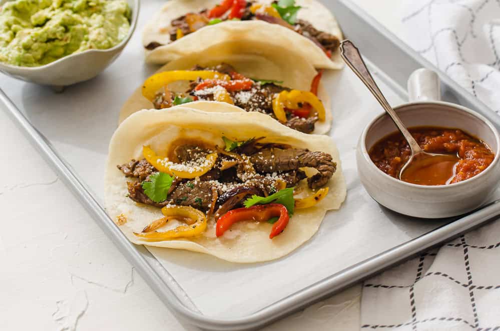 up close shot of steak fajitas lined up on a tray with salsa and guacamole on the side