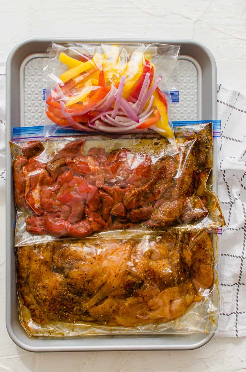 Fajita freezer meal kit with baggies of marinating chicken, marinating steak, and a third one with sliced peppers and onions.