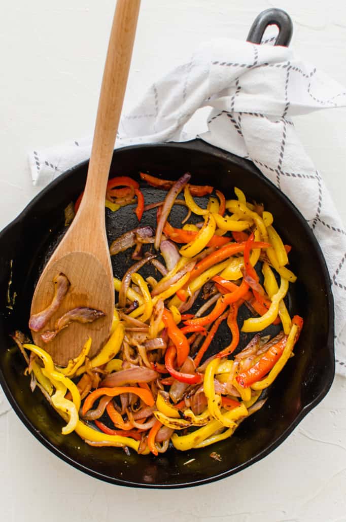 fajita veggies in a cast iron skillet with wooden spoon for serving