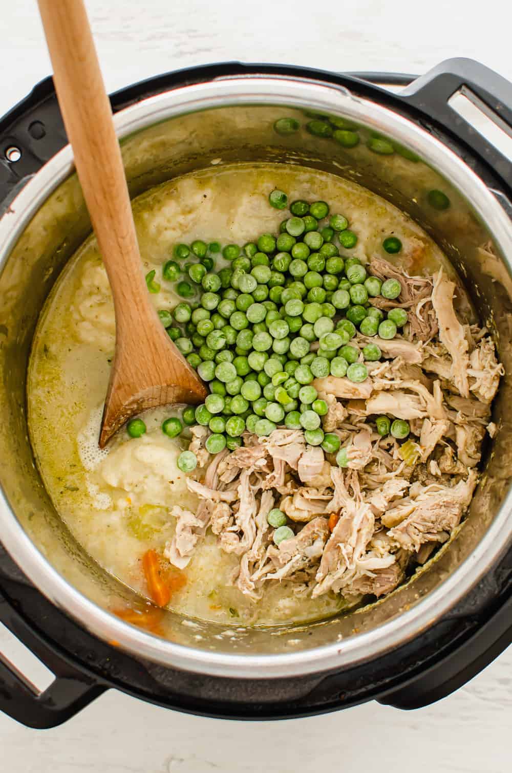 Frozen peas and shredded chicken being added to Instant Pot Chicken and Dumplings.