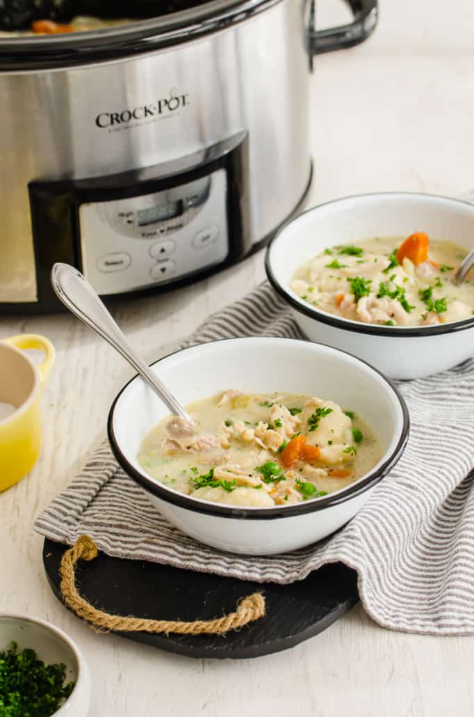 two bowls of chicken and dumplings in front of a crock pot