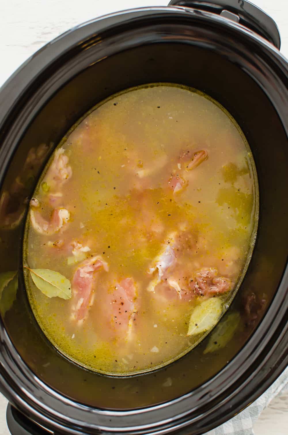 Broth, chicken, and seasonings in slow cooker for chicken and dumplings.