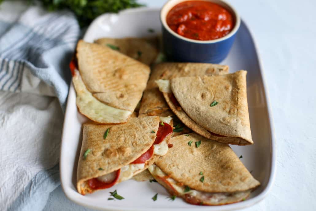 pizza quesadilla triangles on a serving platter with a bowl of marinara sauce for dipping