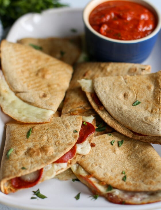 Pizza quesadillas on a square platter with a small bowl of pizza sauce for dipping.