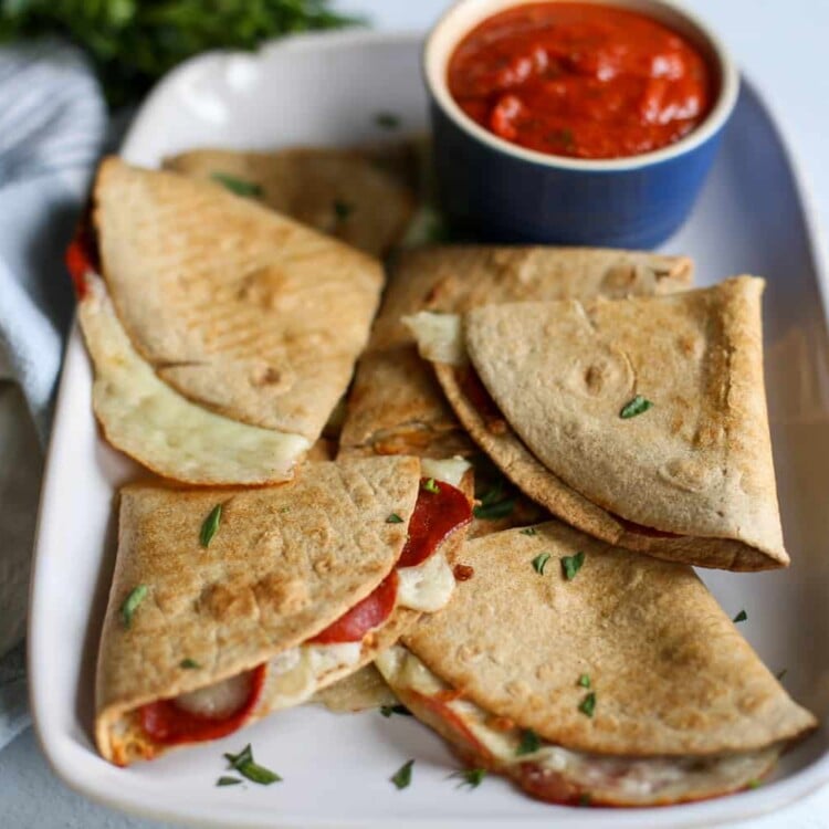 Pizza quesadillas on a square platter with a small bowl of pizza sauce for dipping.