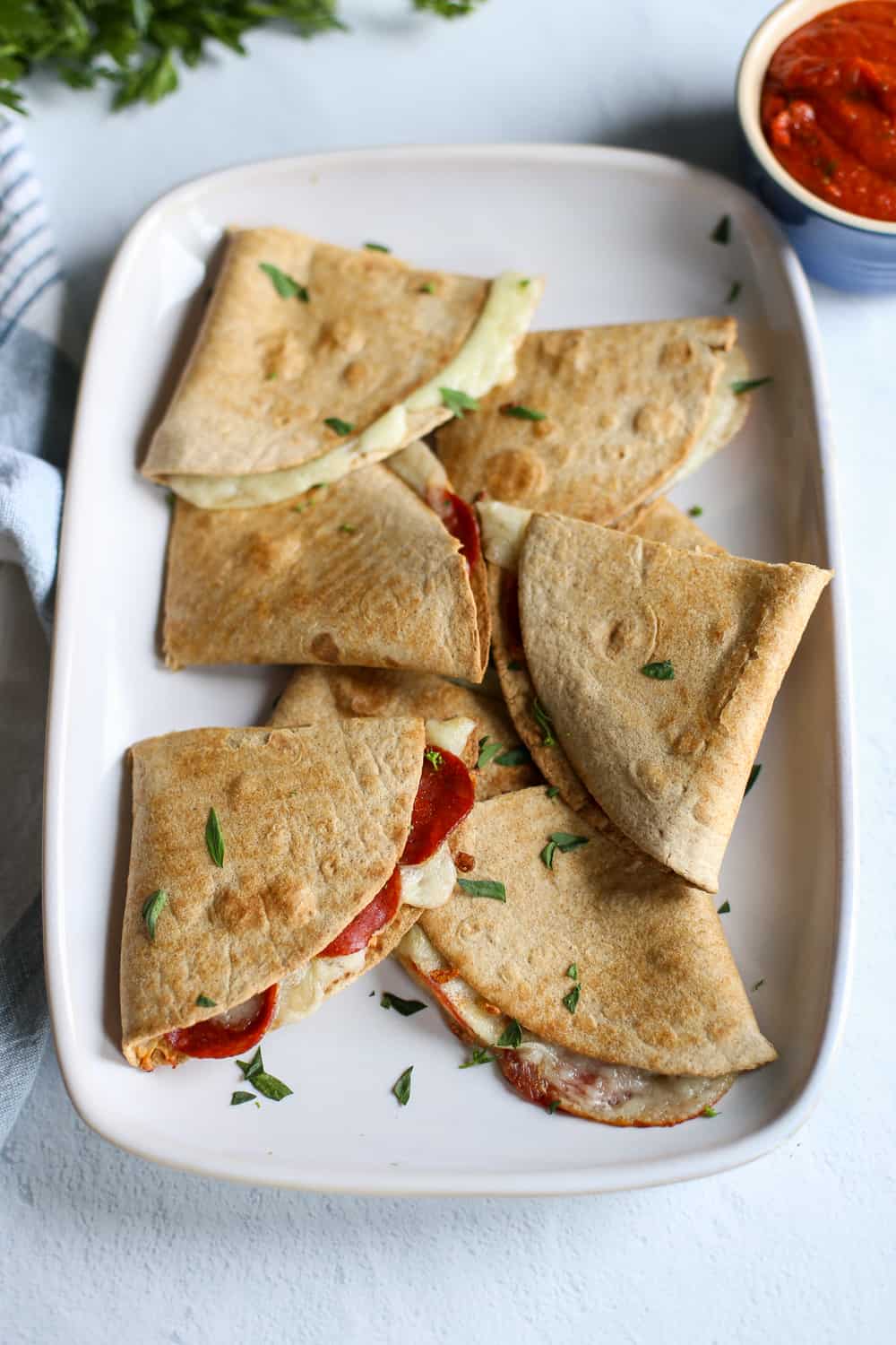 Pizza quesadillas on a platter with a small bowl of pizza sauce on the side.