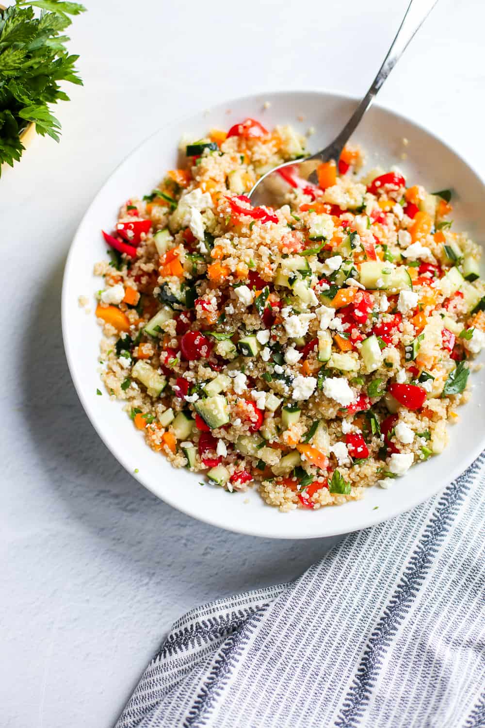 Quinoa tabbouleh salad with a serving spoon in a white bowl.