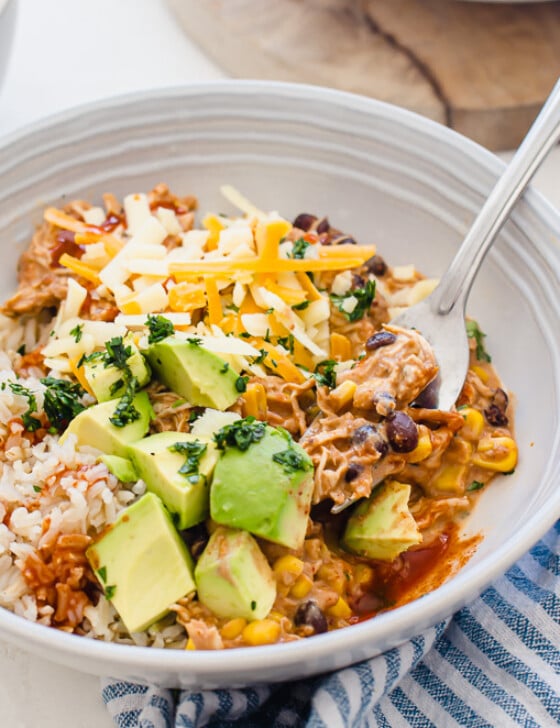 horizontal side shot of plated crockpot mexican chicken in a bowl with a fork with toppings