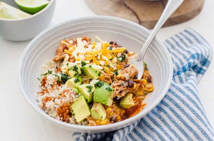 horizontal side shot of plated crockpot mexican chicken in a bowl with a fork with toppings