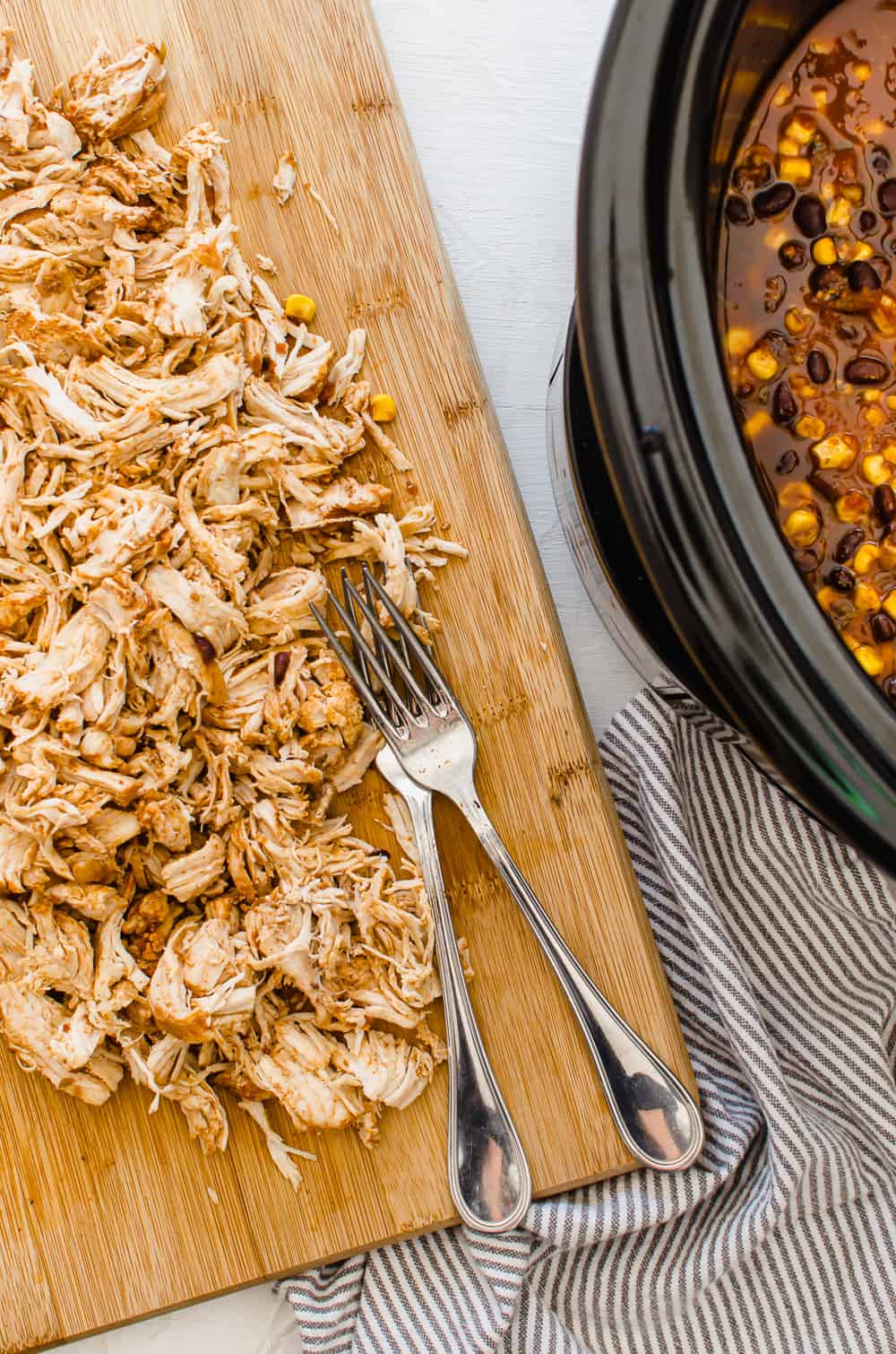 Shredded chicken on a wooden cutting board next to crockpot.