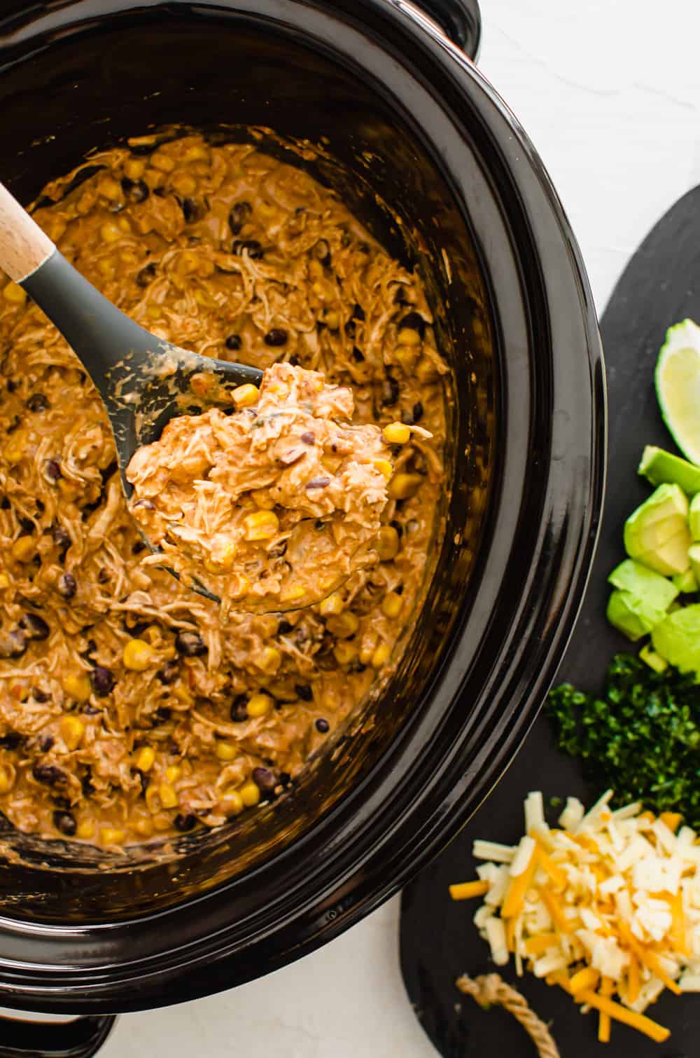 Crockpot Mexican chicken ready to be served from the crockpot with a wooden spoon lifting some out.