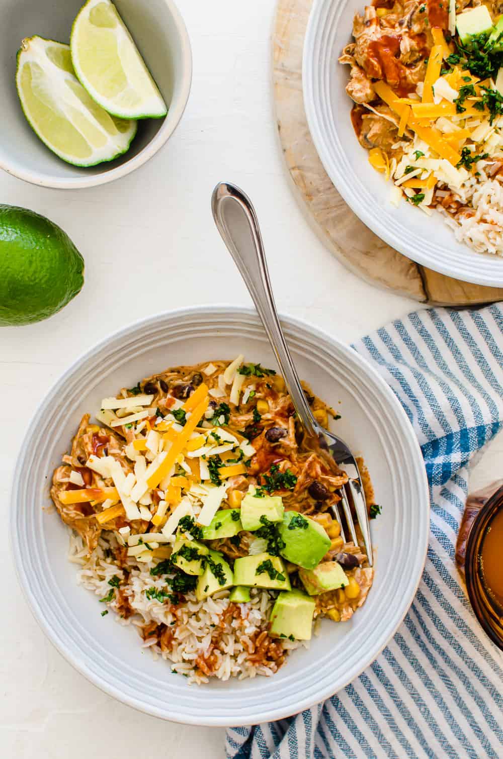 Crockpot Mexican chicken in bowls over rice with shredded cheese, and chopped avocado and cilantro on top.