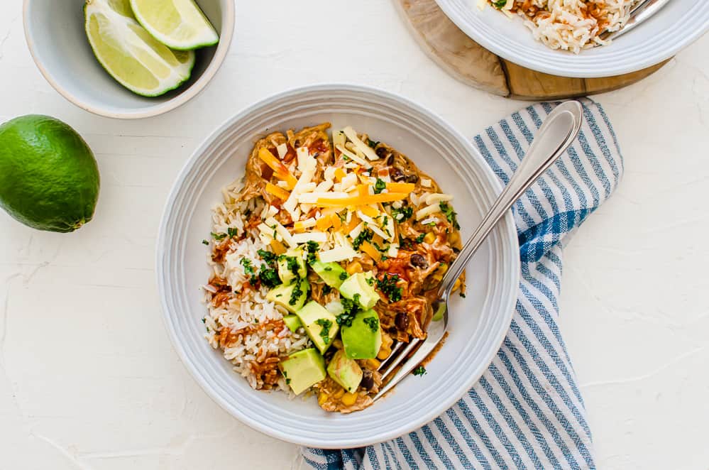 overhead shot of plated crockpot mexican chicken in a bowl with a fork with toppings