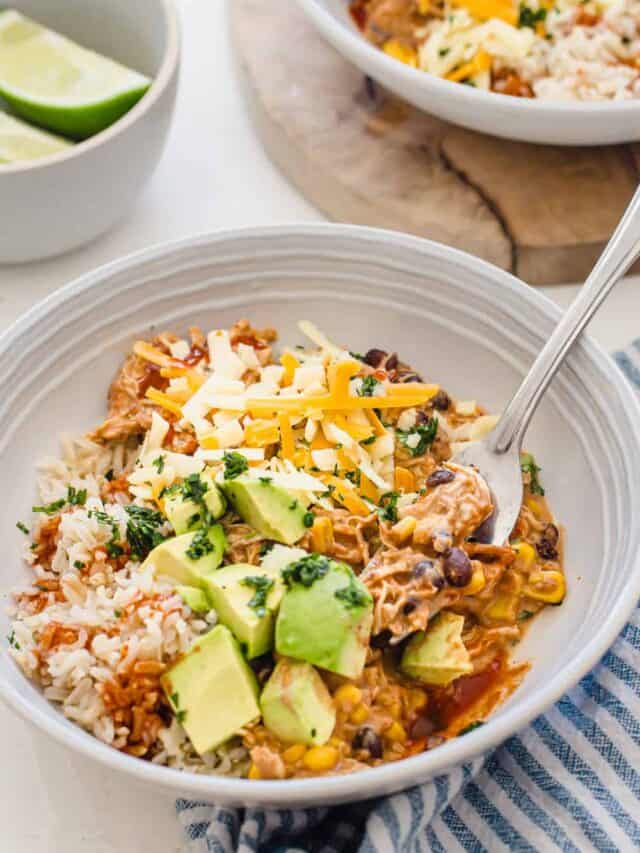 side shot of plated crockpot mexican chicken in a bowl with a fork with toppings