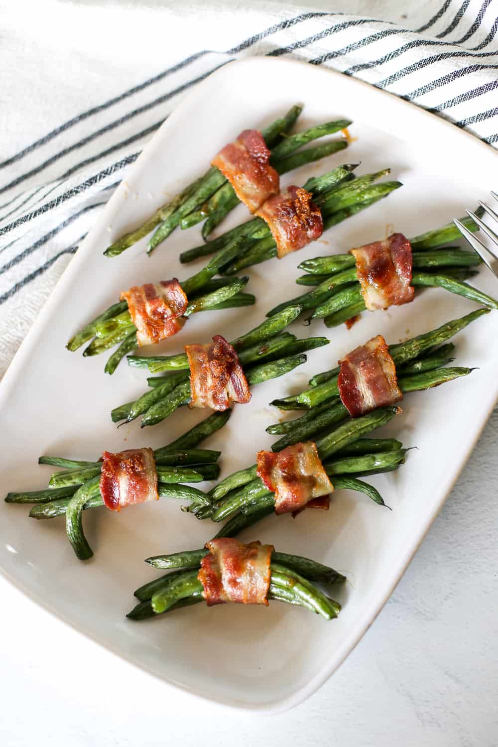 Green beans wrapped in bundles with bacon on a white serving platter.