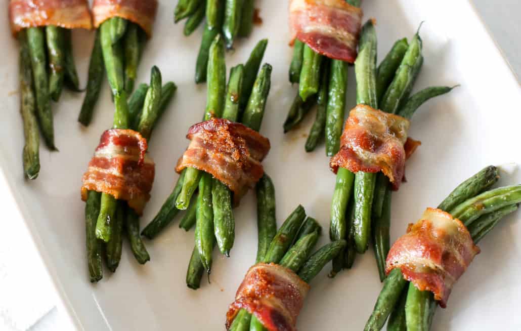 Bacon wrapped green bean bundles on a white platter. 