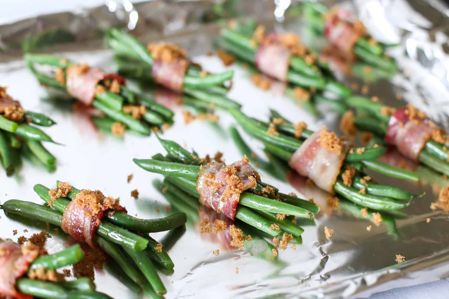 Green beans wrapped in bacon, brushed with garlic butter, and sprinkled with brown sugar before being baked.