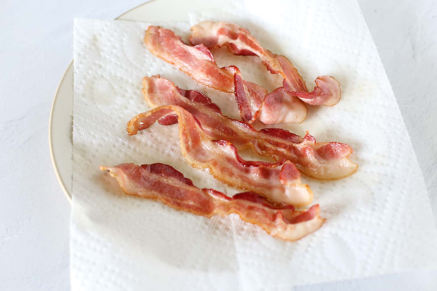Partially cooked bacon on a paper towel on a plate.