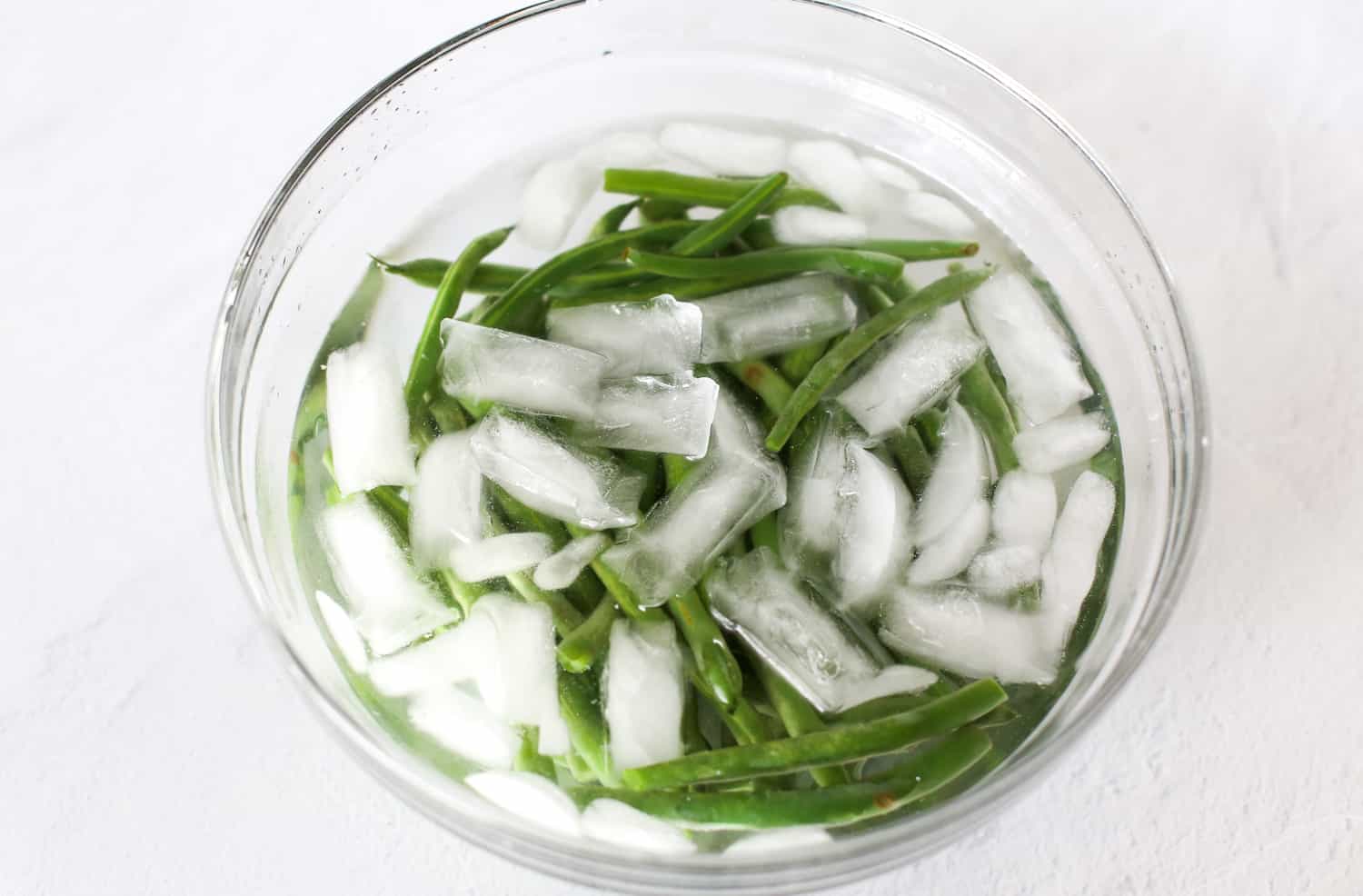 Fresh green beans in a bowl of ice water after being parboiled.